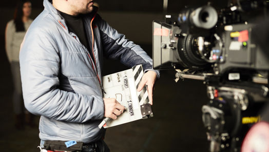 Person stands in front of a camera with a clapperboard
