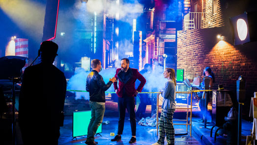 Crew in front of a screen showing the back of an alley