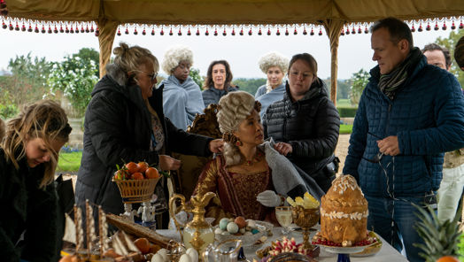 Behind-the-scenes image on the set of Bridgerton filming an outdoor feast in full costume