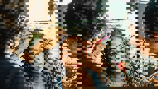 A woman sits in a chair while hair and makeup artists work with her