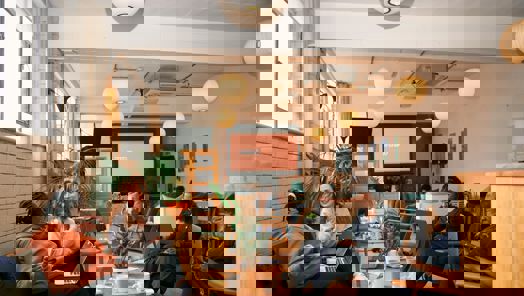 A group of people sit around a table in a cafe working on laptops