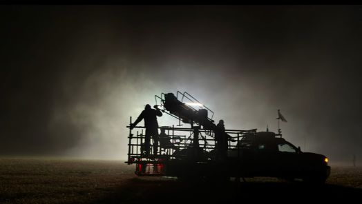 A crew operates a crane grip on the back of a truck during a night-time scene