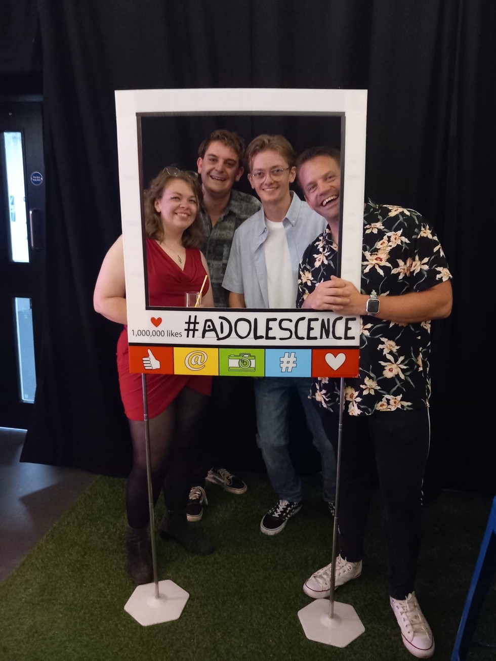 Four crew members smile as they stand behind a cardboard cut out designed to look like an Instagram post with the production name, Adolescence, written underneath