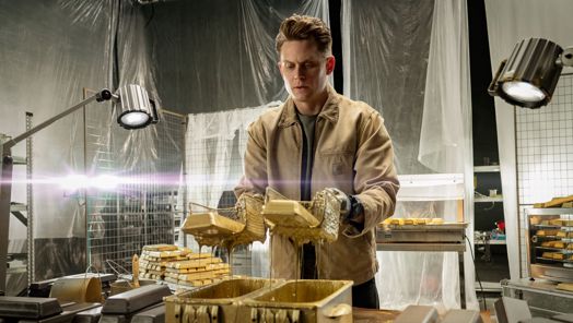 Billy Magnussen as Magnus holding dripping bars of gold on the set of Lift