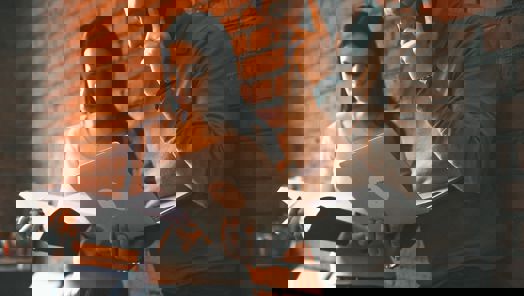 two colleagues working, one speaking on the phone while looking at a laptop and one taking notes on a notebook