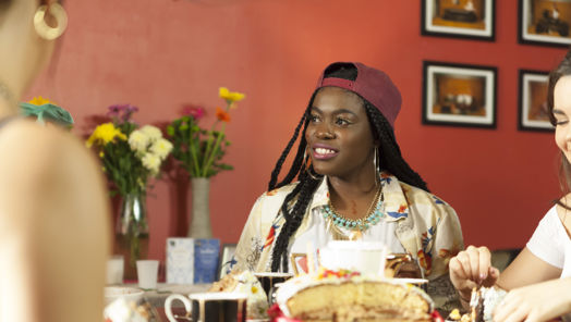 Woman sits at a round coffee table with tea and cake