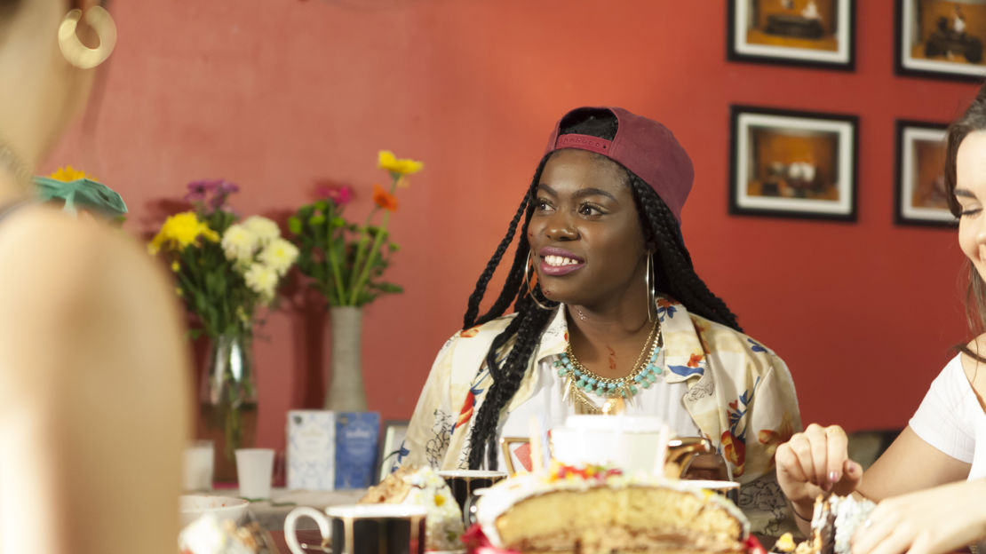 Woman sits at a round coffee table with tea and cake