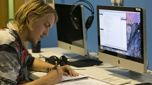 Man writing on a document in front of a computer screen
