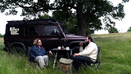 Hosts of The Repair Shop on the Road, Lucia and Dom, sit in a field by a vehicle