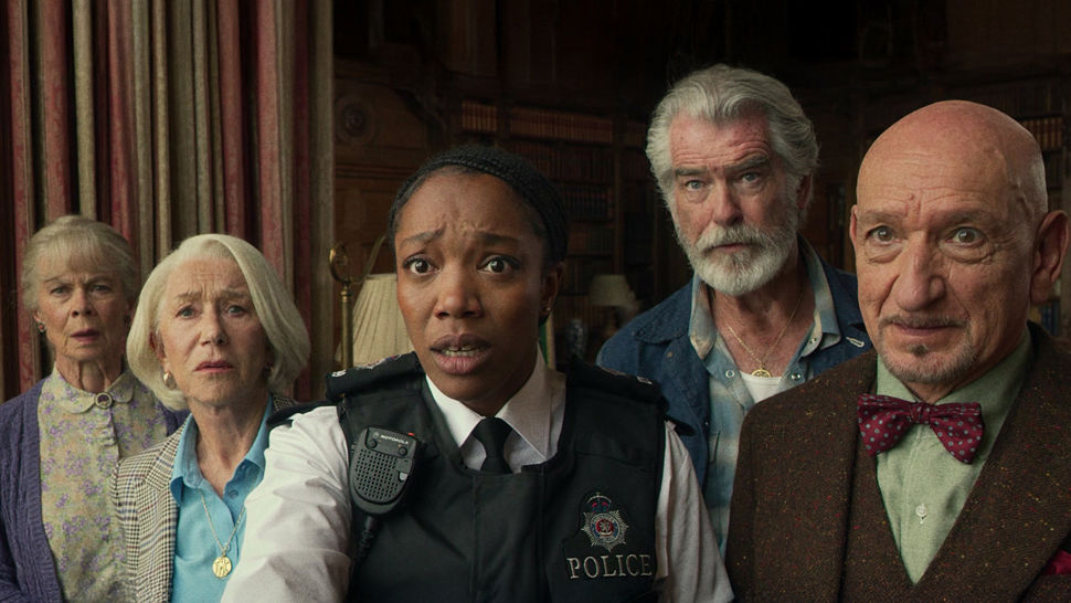 A group of older men and women and a policewoman stand staring, shocked at something behind the screen