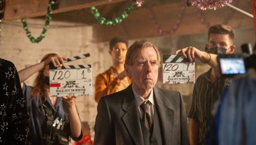 Actor stands in front of a camera while two people are holding clappers