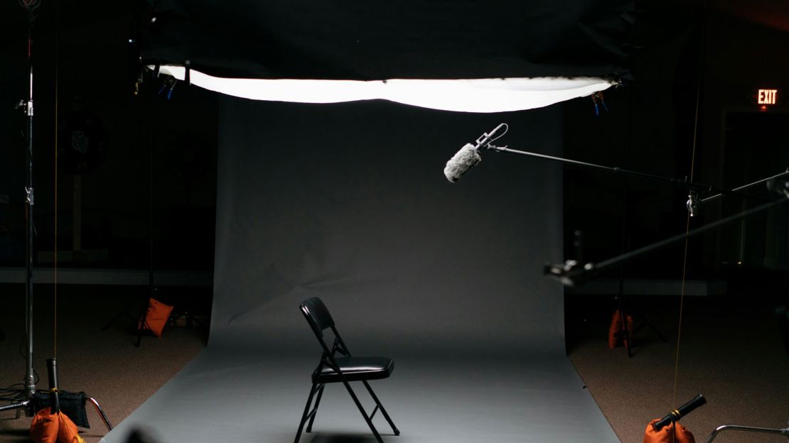 A fold up chair in the centre of a studio with a boom microphone pointing down from above
